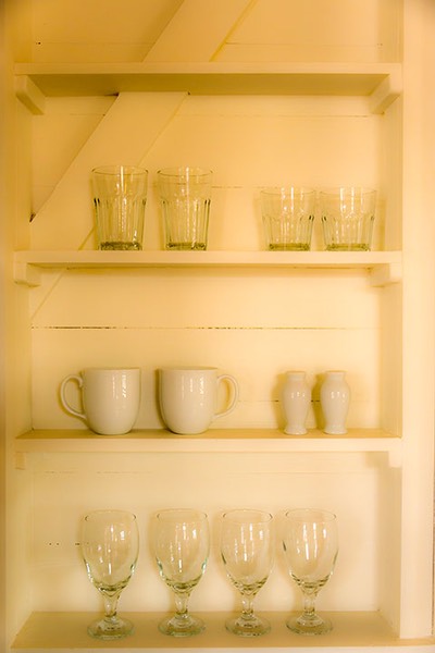 Dream Suite kitchen shelving filled with simple glasses and white ceramic cups and shakers is carved into the boarded walls at Mahogany Bay Village on Ambergris Caye in Belize