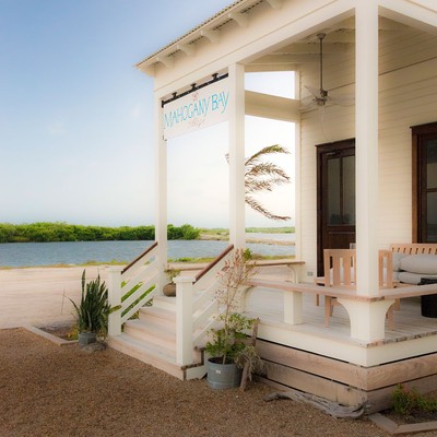 whitewashed front porch with weathered mahogany trimmings sits in the tropical breeze at the edge of Mahogany Bay Village on Ambergris Caye in Belize