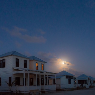 Ambergris Caye moonrise over Mahogany Bay Village with twin cottage windows glowing orange from the second level as the rest of the village street sleeps in Belize