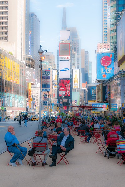 New Yorkers sitting astride red folding chairs in Times Square, on a plaza recently reclaimed by the Tactical Urbanists